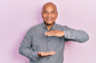 Orta yaşlı, gündelik kıyafetler giyen, büyük ve büyük beden işareti gösteren el kol hareketleri yapan Latin bir adam. Ölçü sembolü. Kameraya bakıp gülümsüyor. ölçüm kavramı. 