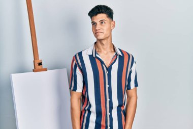 Genç İspanyol adam boş tuvale yakın duruyor gülümsüyor ve yan tarafa bakıyor ve düşünüyor.. 