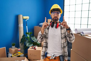 Sakallı, ev tadilatında çalışan, üzgün ve üzgün görünen, yönünü parmaklarıyla gösteren mutsuz ve depresif bir İspanyol.. 