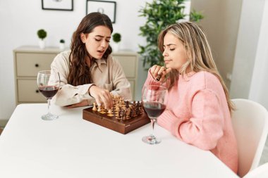 Evde satranç oynayan genç bir çift kırmızı şarap içiyor..