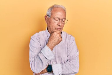 Gri saçlı, şık gömlekli ve gözlüklü yaşlı adam kollarını kavuşturarak depresyondan sıkılmış ve yorgun göründüğünü düşünüyor.. 