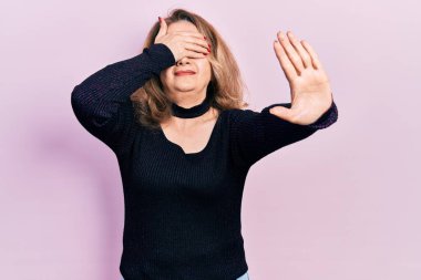 Orta yaşlı beyaz kadın gündelik giysiler giyip elleriyle gözlerini kapatıyor ve üzgün ve korku ifadeleriyle dur hareketi yapıyor. utangaç ve olumsuz kavram. 