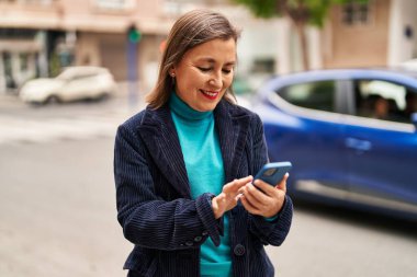 Sokakta akıllı telefon kullanan orta yaşlı bir iş kadını.