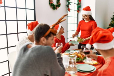 Bir grup genç, mutlu bir şekilde gülümseyerek evde Noel yemeği yiyor..