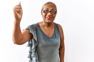 Mature hispanic woman wearing glasses standing over isolated background angry and mad raising fist frustrated and furious while shouting with anger. rage and aggressive concept. 