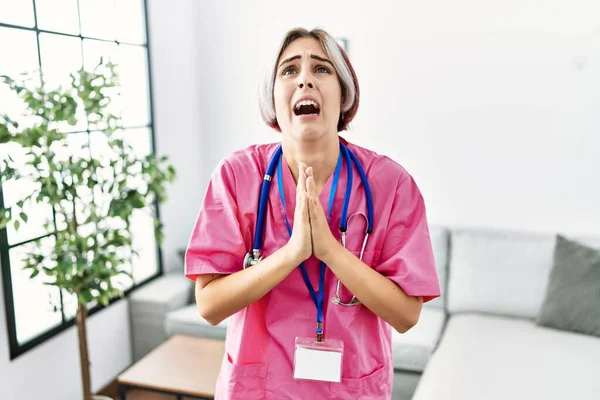 Young Beautiful Woman Wearing Doctor Uniform Stethoscope Begging Praying Hands - Stock-foto