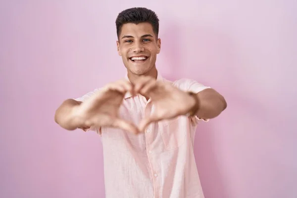 Молодой Латиноамериканец Стоящий Розовом Фоне Улыбающийся Любви Делает Символическую Форму — стоковое фото