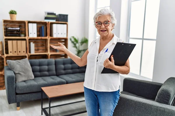 Senior grey-haired woman psychologist holding clipboard at psychology center