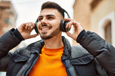 Sakallı yakışıklı, neşeli ve kendine güvenen, kışlık palto ve kulaklık takan bir İspanyol.