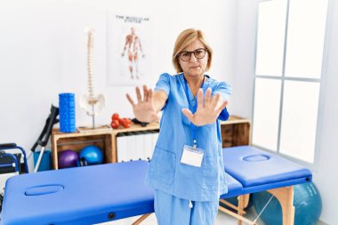 Orta yaşlı sarışın kadın ağrı kesici kliniğinde çalışıyor. Korkudan dehşete düşmüş ve korkmuş. El hareketlerini durdur, şok içinde bağır. panik konsepti. 