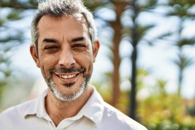 Orta yaşlı, kır saçlı, gülümseyen bir adam şehirde mutlu bir şekilde duruyor..