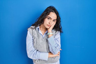 Mavi arka planda duran esmer kadın kollarını kavuşturarak depresyondan sıkılmış ve yorgun görünüyor.. 