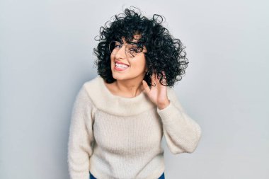 Young middle east woman wearing casual white tshirt smiling with hand over ear listening an hearing to rumor or gossip. deafness concept. 