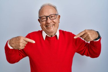 Gri saçlı yaşlı adam izole edilmiş arka planda duruyor. Yüzünde bir gülümsemeyle kendinden emin görünüyor. Kendini gururlu ve mutlu bir şekilde gösteriyor.. 