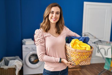 Young woman holding laundry basket with a happy and cool smile on face. lucky person. 