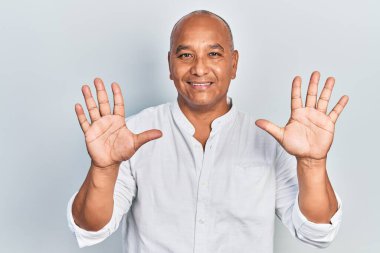 Orta yaşlı, gündelik kıyafetler giyen Latin bir adam on numarayı gösterip işaret ederken kendinden emin ve mutlu bir şekilde gülümsüyor.. 