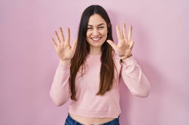 Pembe arka planda duran genç esmer kadın dokuz numarayı gösterip işaret ederken kendinden emin ve mutlu bir şekilde gülümsüyor.. 