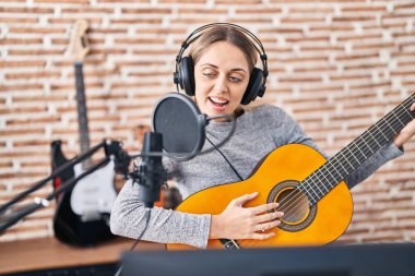 Genç kadın sanatçı müzik stüdyosunda klasik gitar çalarak şarkı söylüyor.