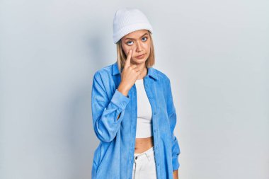 Yün şapka takan güzel sarışın kadın senin jestini izliyor, şüpheli bir ifade. 