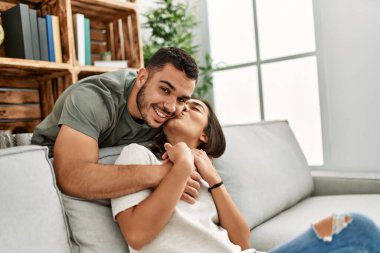 Kanepede oturan genç latin çift evde sarılıyorlar..