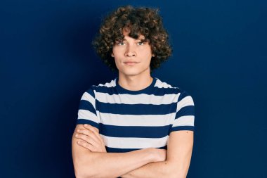 Sıradan çizgili tişört giyen yakışıklı genç adam şüpheci ve gergin, yüzünde çapraz kollu tasvip etmeyen yüz ifadesi. negatif kişi. 