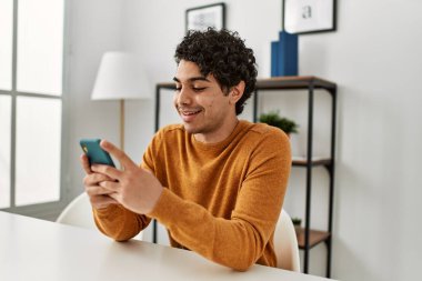 Genç İspanyol adam akıllı telefon kullanıyor. Evdeki masada oturuyor..