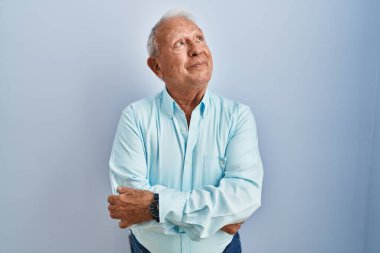 Mavi arka planda gri saçlı yaşlı adam gülümsüyor, yan tarafa bakıyor ve düşünüyor.. 