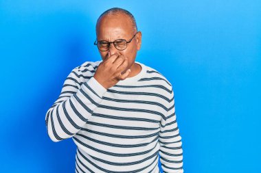 Orta yaşlı, sıradan kıyafetler ve gözlük takan Latin bir adam pis ve iğrenç bir koku alıyor. Nefesini burnu havada tutuyor. Kötü kokuyor. 