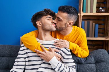 İki erkek birbirine sarılıyor ve evdeki koltukta öpüşüyorlar.