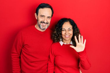 Middle age couple of hispanic woman and man hugging and standing together showing and pointing up with fingers number five while smiling confident and happy. 