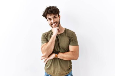Hispanic man standing over isolated white background with hand on chin thinking about question, pensive expression. smiling and thoughtful face. doubt concept. 