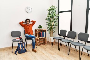 Genç İspanyol adam, bekleme odasında müzik dinlerken kendinden emin bir şekilde gülümsüyor.