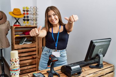 Perakende dükkanında elinde açık metinle afiş tutan genç esmer kadın el hareketleriyle olumlu jest yapmayı onaylıyor, gülümsüyor ve başarı için mutlu. kazanan jest. 