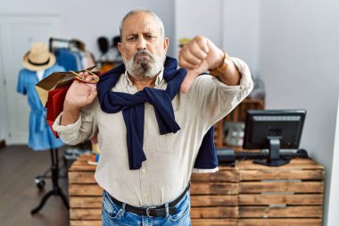 Butik dükkanında alışveriş torbaları tutan yakışıklı bir adam mutsuz ve sinirli görünüyor reddedilmiş ve olumsuz bir hareket yapıyor. kötü ifade. 