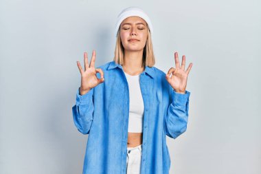 Güzel sarışın kadın yün şapka takıyor rahatlamış ve gözleri kapalı gülümsüyor parmaklarıyla meditasyon hareketi yapıyor. yoga konsepti. 
