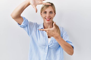 Beyaz arka planda duran güzel sarışın kadın gülümsüyor ve mutlu yüzlü eller ve parmaklarla çerçeve yapıyor. yaratıcılık ve fotoğrafçılık kavramı. 