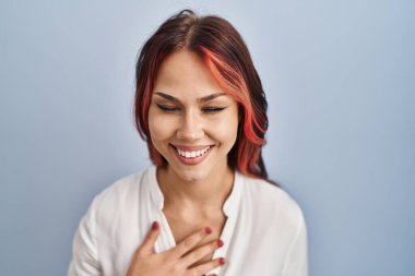 İzole edilmiş arka planda günlük beyaz tişört giyen genç beyaz bir kadın. Gülerek kahkahalarla gülüyor. Çünkü elleri vücutta olan komik bir şaka.. 