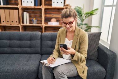 Psikoloji merkezindeki koltukta oturan akıllı telefon kullanan genç sarışın kadın psikolog.