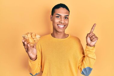 Genç Afro-Amerikalı adam elinde patates cipsi tutarken mutlu bir şekilde gülümsüyor. 