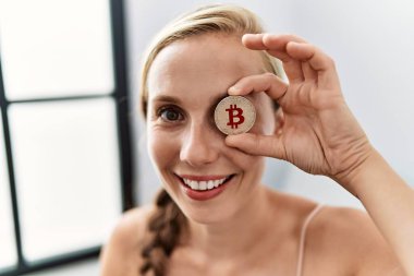 Evdeki kanepede oturan bitcoin ove gözü tutan beyaz bir kadın.