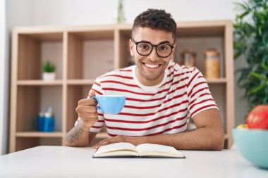 Afro-Amerikalı adam kitap okuyor, evde kahve içiyor.