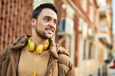 Şehirde kulaklık takarak mutlu gülümseyen genç İspanyol adam..