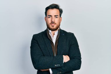 Sakallı, kollarını kavuşturmuş yakışıklı beyaz adam yüzünde ciddi bir ifadeyle rahatlamış. Basit ve doğal bir şekilde kameraya bakıyorsun.. 