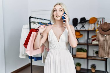 Alışveriş torbaları tutan beyaz bir kadın giyim mağazasında akıllı telefondan konuşuyor.