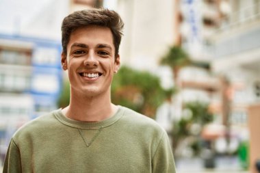 Genç İspanyol adam gülümseyerek şehirde mutlu mesut dikiliyor..