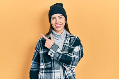Beautiful woman with blue eyes wearing wool cap smiling cheerful pointing with hand and finger up to the side 