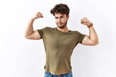 Hispanic man standing over isolated white background showing arms muscles smiling proud. fitness concept. 