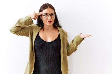 Genç esmer kadın izole edilmiş arka planda duruyor. Avuç içinin açık olmasından rahatsız ve kafası karışık. Kopya alanını gösteriyor ve alnını işaret ediyor. Bunu bir düşün.. 