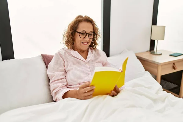 中年白人妇女坐在卧室的床上看书 — 图库照片