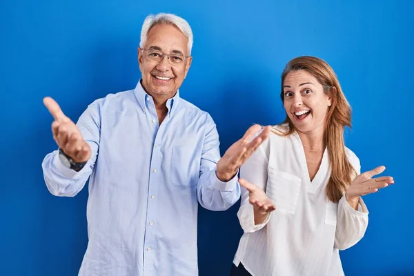 Middle Age Hispanic Couple Standing Blue Background Smiling Cheerful Offering — Stockfoto